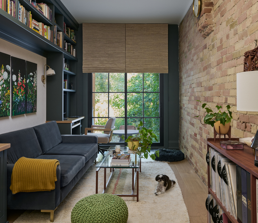 Woven wood shades on black trim windows in a narrow den with built-in shelving